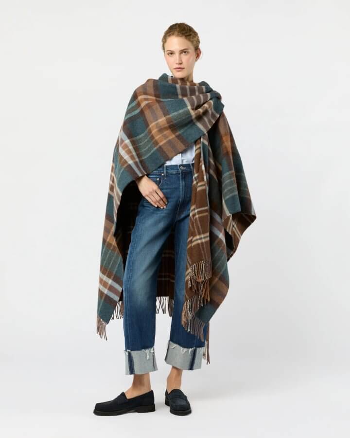 23 Luxurious Nashville FINDS for Holiday 2025 - 2 Person standing against a white background, wearing luxe blue jeans with frayed cuffs, a white shirt, black loafers, and a large brown and blue plaid shawl draped over their shoulders—perfect for a cozy holiday look.