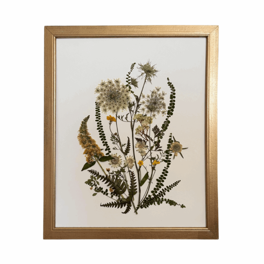 A framed artwork displays an arrangement of pressed and dried wildflowers and greenery on a white background, bordered by a luxe gold-colored frame—a perfect touch for your Nashville holiday décor.