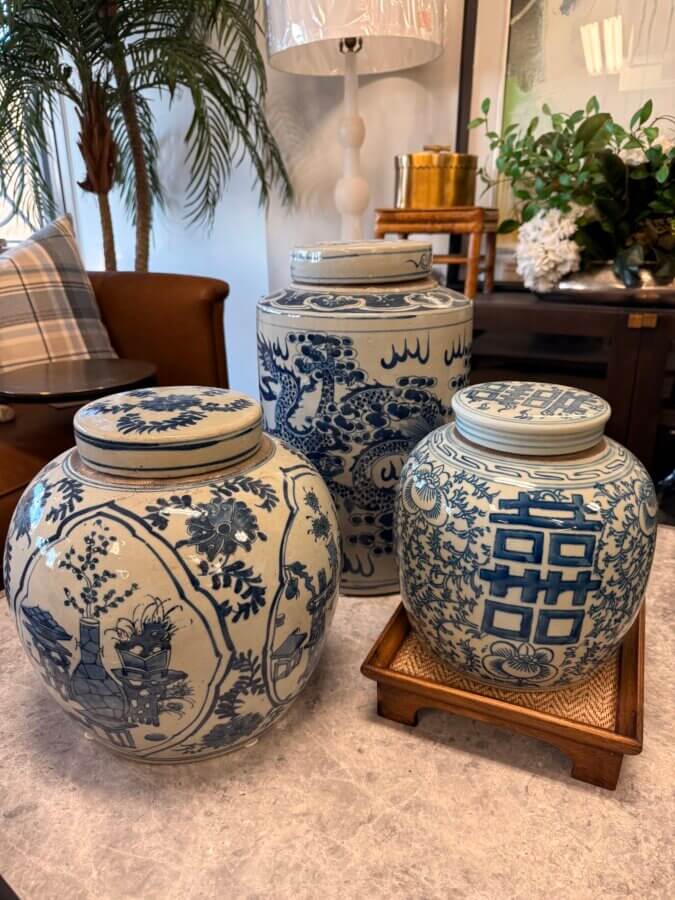 23 Luxurious Nashville FINDS for Holiday 2025 - 21 Three blue and white ceramic jars with intricate designs are displayed on a table, two on a marble surface and one on a wooden tray, creating a luxe living room setting with plants and decor—perfect for the holiday season.