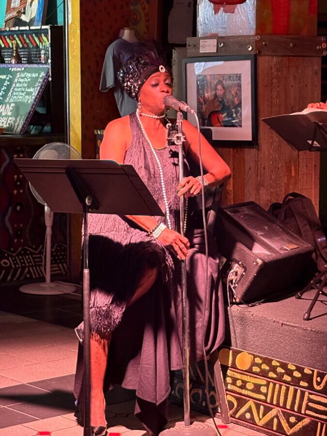 Meet Memphis Jazz Musician Cequita Monique - 5 Cequita Monique, dressed in a vintage-style dress and headpiece, performs on stage at FACES, holding a microphone, with music stands and colorful decor in the background.