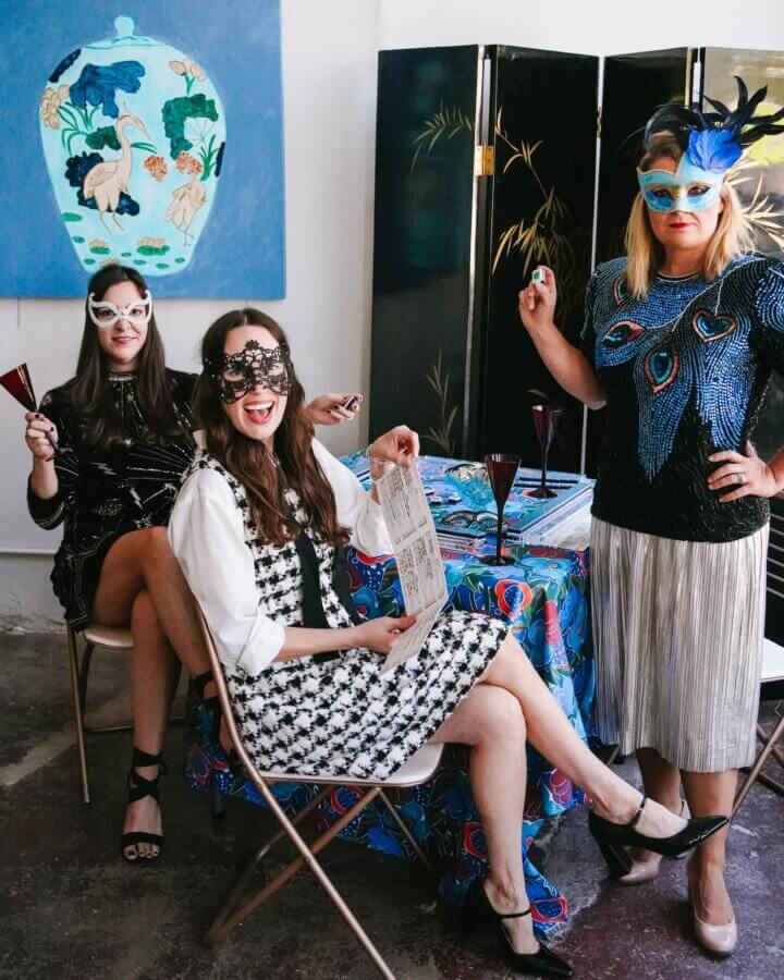 Meet the Owners of Memphis's New Elevated Vintage Shop: Heirloom House - 6 Three women, including Alice Kerley and Dorothy Collier, wearing decorative FACES masks, sit around a table with drinks and a menu, posing for a photo in an art-filled room with colorful decor.