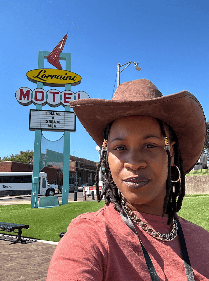 Meet the Woman Behind the New Memphis Rap Tour - 2 Taylor Nicole Barksdale, wearing a brown cowboy hat, stands in front of the Lorraine Motel sign displaying "HAVE DREAM MLK" on a clear, sunny day.