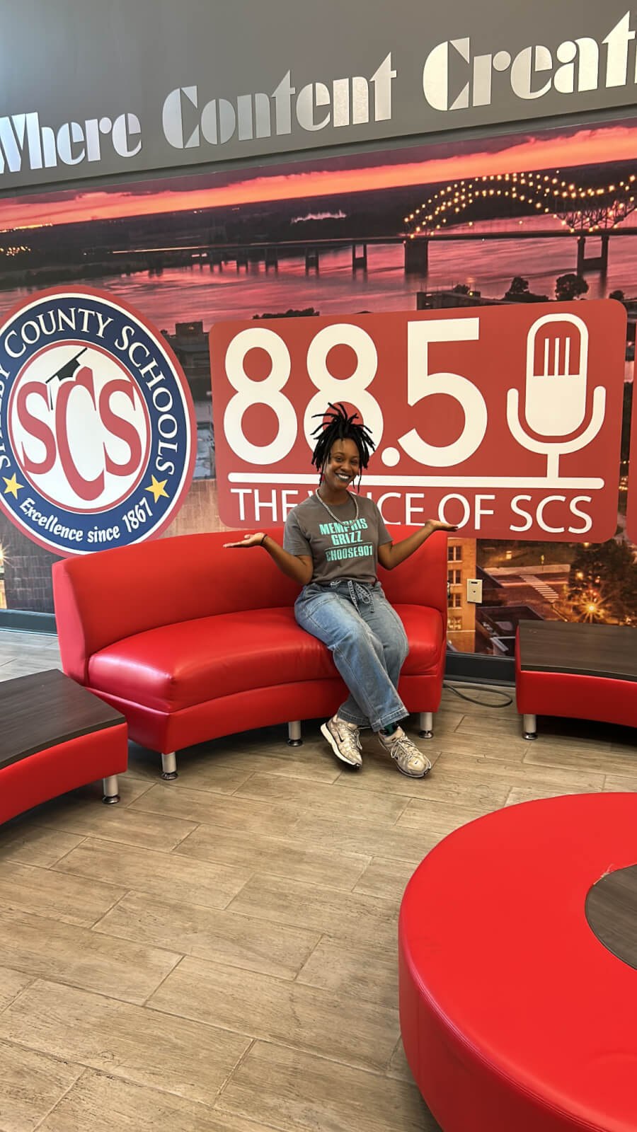 Meet the Woman Behind the New Memphis Rap Tour - 3 Taylor Nicole Barksdale sits on a red couch in front of a wall featuring the 88.5 FM radio logo and the Shelby County Schools emblem.