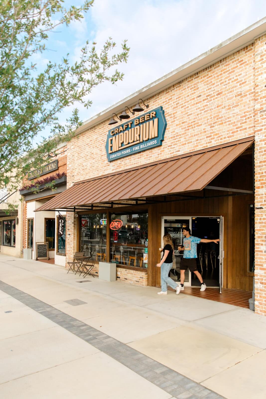 12 Florida Food & Heritage Trails Worth Traveling For - 11 Two people enter a brick building with a sign reading "Craft Beer Emporium," perfect for travel enthusiasts exploring heritage trails and sampling local Florida food. The storefront has large windows, metal awnings, and an "Open" sign.