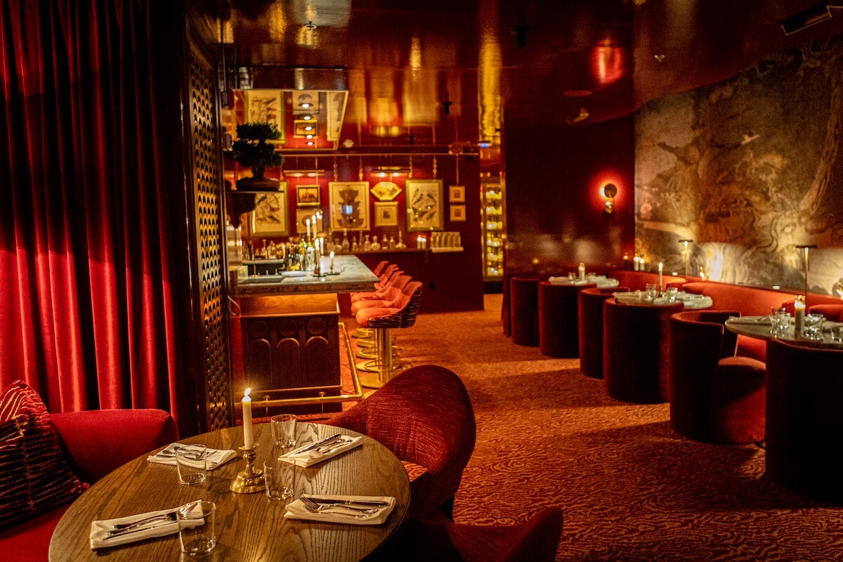 Upscale restaurant interior with red velvet seating, dim lighting, a set dining table in the foreground, and an Oxford cocktail bar—this must-visit spot offers a touch of miscellanea in its chic ambiance.