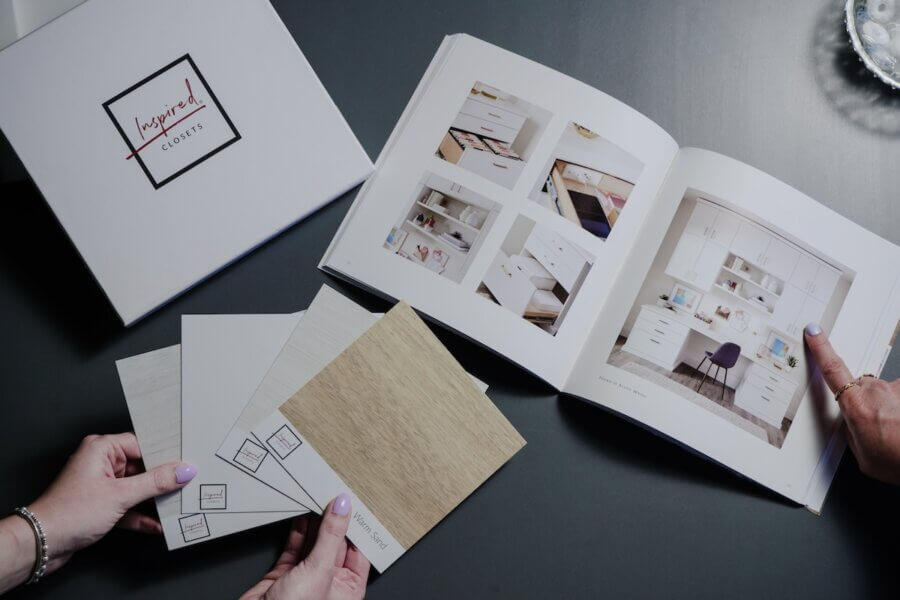 Custom Organization Ideas Homeowners Are Loving Right Now - 7 Two homeowners review design samples and color swatches alongside a catalog displaying closet organization systems on a dark table, gathering inspiration and organization ideas for home organization projects.