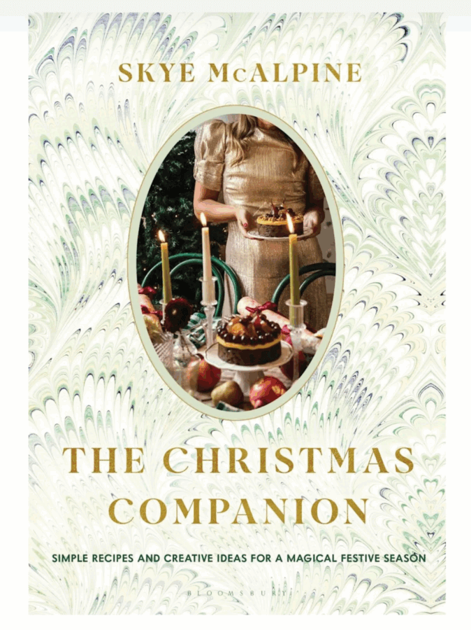 50 Under $50: Your Nashville Holiday Gift Guide - 12 The cover of "The Christmas Companion" by Skye McAlpine, featured in our Holiday Gift Guide, shows a person in a gold dress setting a festive table with candles, fruit, and cakeβperfect inspiration for gifts under $50.