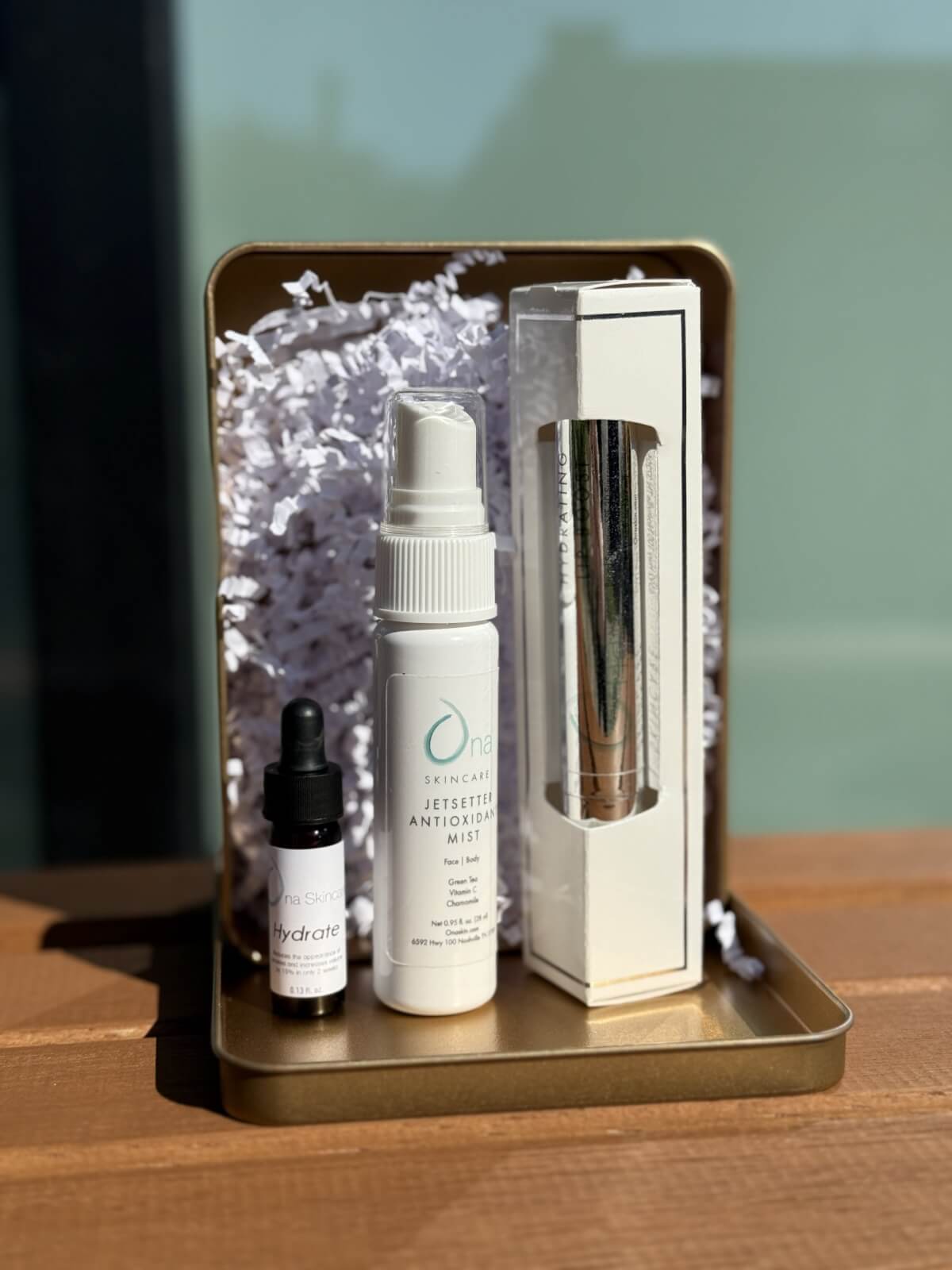 50 Under $50: Your Nashville Holiday Gift Guide - 37 A small gold tray holds a dropper bottle, a mist spray labeled "Jetsetter Antioxidant Mist," and a boxed item on white shredded paperβperfect for Nashville-inspired gifts under $50.