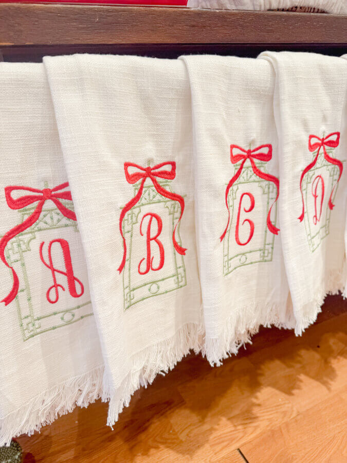 50 Under $50: Your Nashville Holiday Gift Guide - 5 White cloth napkins with red and green embroidered letters A, B, C, and Dβeach topped with a red bowβhang in a row over wood. Perfect for Gifts Under $50, they're a festive pick for any Nashville Holiday Gift Guide.
