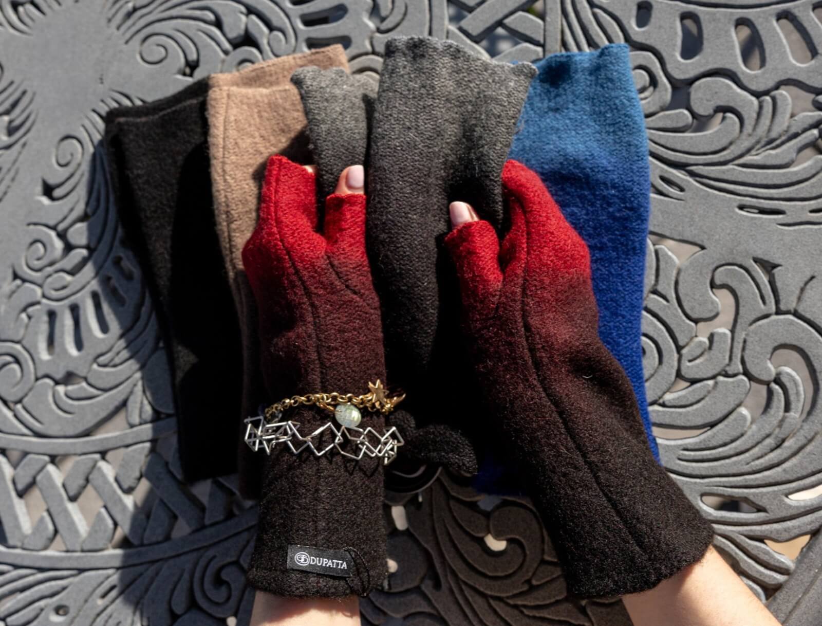 50 Under $50: Your Nashville Holiday Gift Guide - 24 A person wearing red and black fingerless gloves displays four pairs of wool gloves in different colors on a decorative metal surfaceβperfect Christmas gifts under $50.