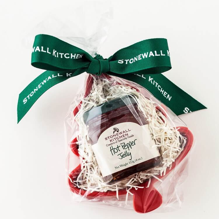 50 Under $50: Your Nashville Holiday Gift Guide - 28 A jar of Stonewall Kitchen Hot Pepper Jelly wrapped in clear plastic with white shred, placed in a red dish, and tied with a green Stonewall Kitchen ribbonβperfect for your Nashville-inspired Holiday Gift Guide.