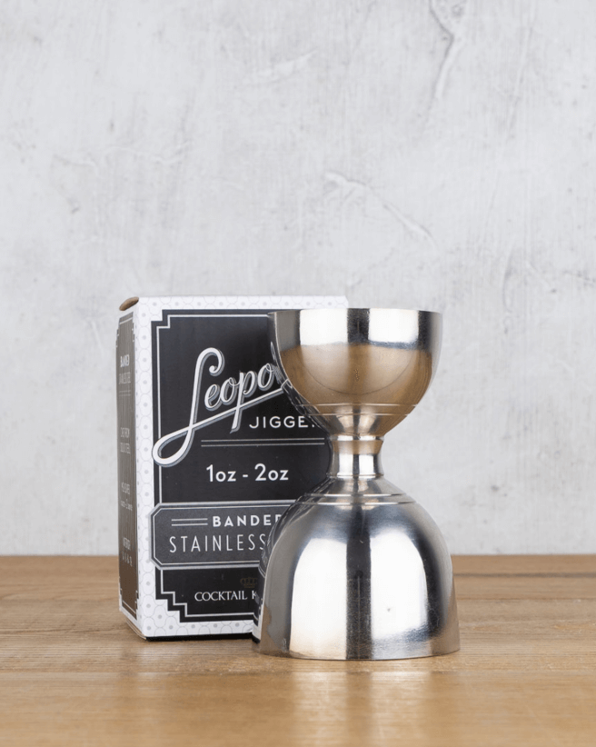 50 Under $50: Your Nashville Holiday Gift Guide - 44 A stainless steel jigger with 1oz and 2oz measurements sits on a wooden surface next to its branded packagingβperfect for Nashville enthusiasts and featured in our Holiday Gift Guide of gifts under $50.