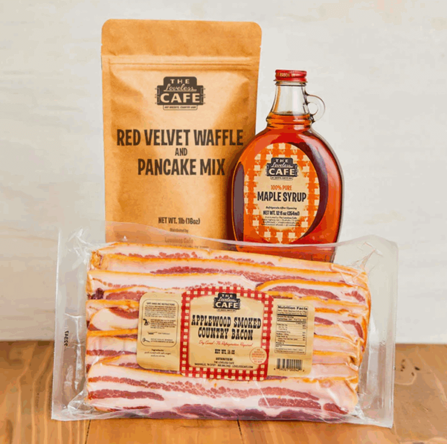 50 Under $50: Your Nashville Holiday Gift Guide - 30 A Nashville-inspired package of red velvet waffle and pancake mix, a bottle of maple syrup, and applewood smoked country bacon makes the perfect addition to any Holiday Gift Guide, displayed on a rustic wooden surface.