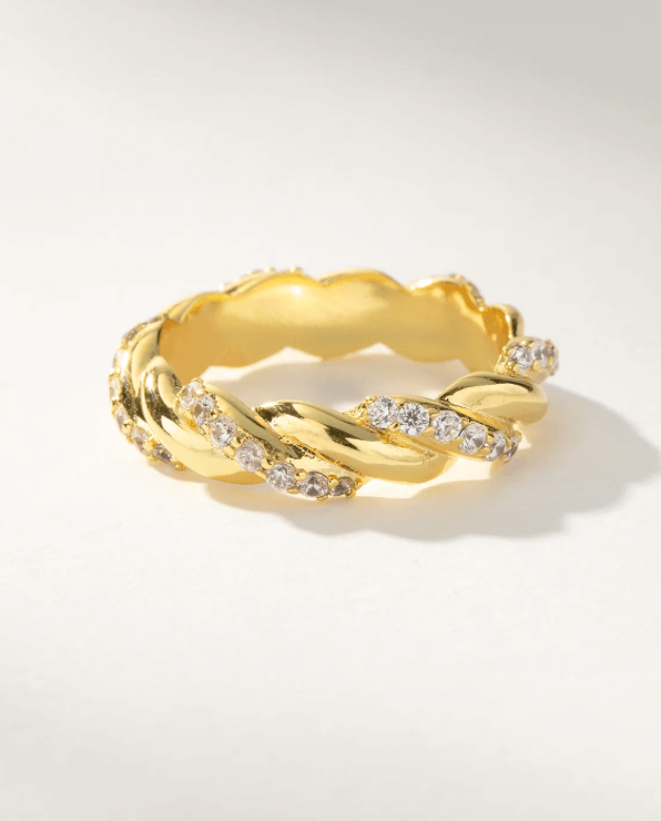 50 Under $50: Your Nashville Holiday Gift Guide - 23 A gold twisted band ring accented with small clear gemstones is shown resting on a light surfaceβan elegant choice for any Nashville jewelry lover, perfect for your Holiday Gift Guide.