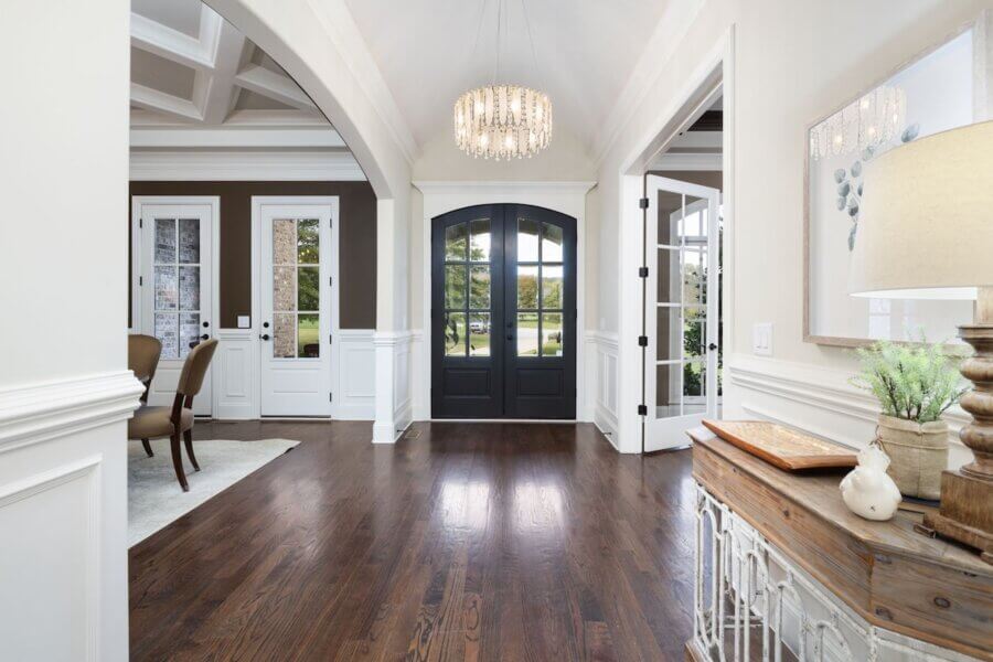 Just Listed! A Franklin Home Where Style & Serenity Coexist - 3 A bright foyer in this Franklin Home features dark double doors, hardwood floors, a chandelier, and a side table; the dining room is visible on the left, with glass-paneled doors on the right—ideal for luxury living.