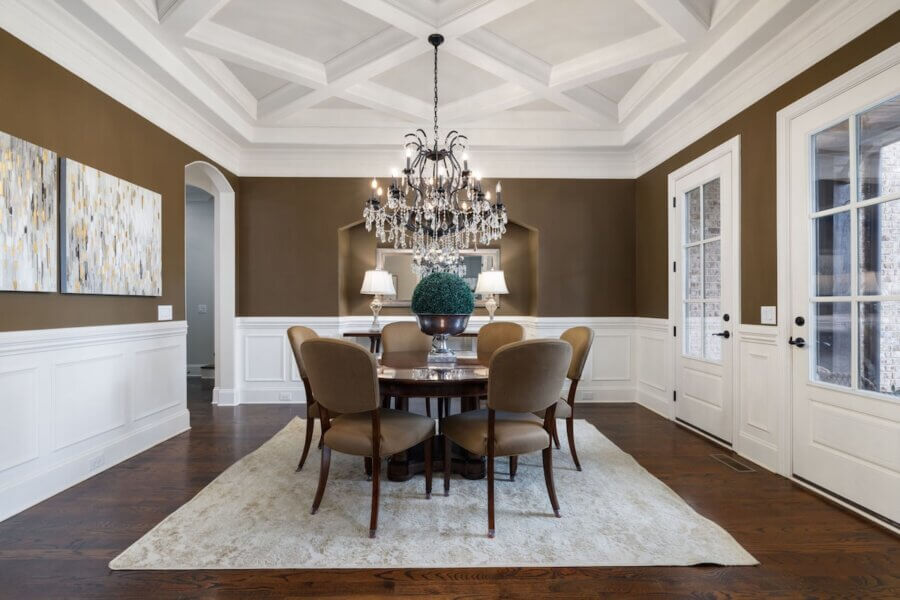Just Listed! A Franklin Home Where Style & Serenity Coexist - 5 Experience luxury living in this formal dining room with a chandelier, round table for six, two wall paintings, brown walls with white trim, and hardwood floors. A plant centerpiece adds a touch of pastoral peace to this elegant Franklin home.