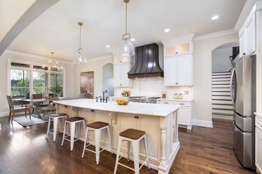 Just Listed! A Franklin Home Where Style & Serenity Coexist - 8 Modern kitchen in a Franklin home with a large island, white cabinets, stainless steel appliances, wooden stools, and hardwood floors; dining area and staircase visible in the background exude luxury living.