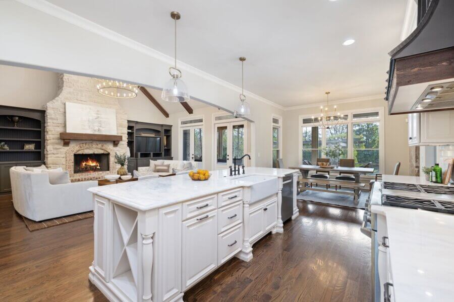 Just Listed! A Franklin Home Where Style & Serenity Coexist - 7 Spacious open-concept kitchen and living area in this Franklin Home features white cabinetry, marble countertops, a farmhouse sink, dining table, hardwood floors, and a stone fireplace—perfect for enjoying luxury living and pastoral peace.