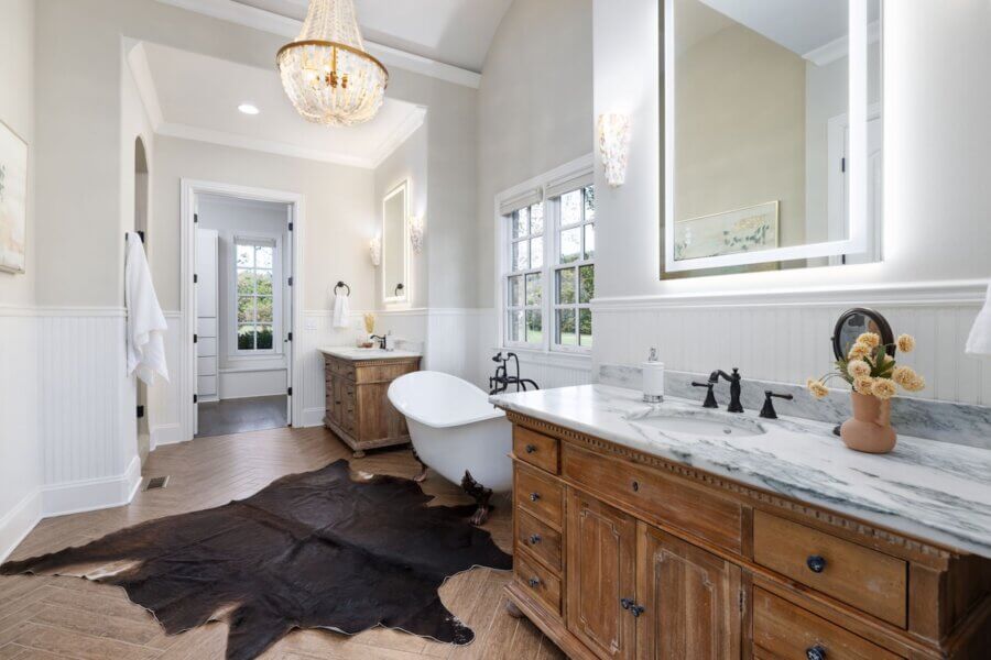 Just Listed! A Franklin Home Where Style & Serenity Coexist - 13 Experience luxury living in this Franklin home’s serene bathroom, featuring a freestanding tub, marble-topped wooden vanities, large mirrors, cowhide rug, chandelier, and neutral tones illuminated by natural light.