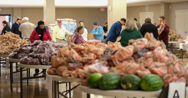 Nashville Toy and Food Drives to Support This Holiday Season - 4 People gather around tables filled with bags of produce and watermelons at an indoor food distribution center in Nashville, supporting the 2025 Holiday Drives.