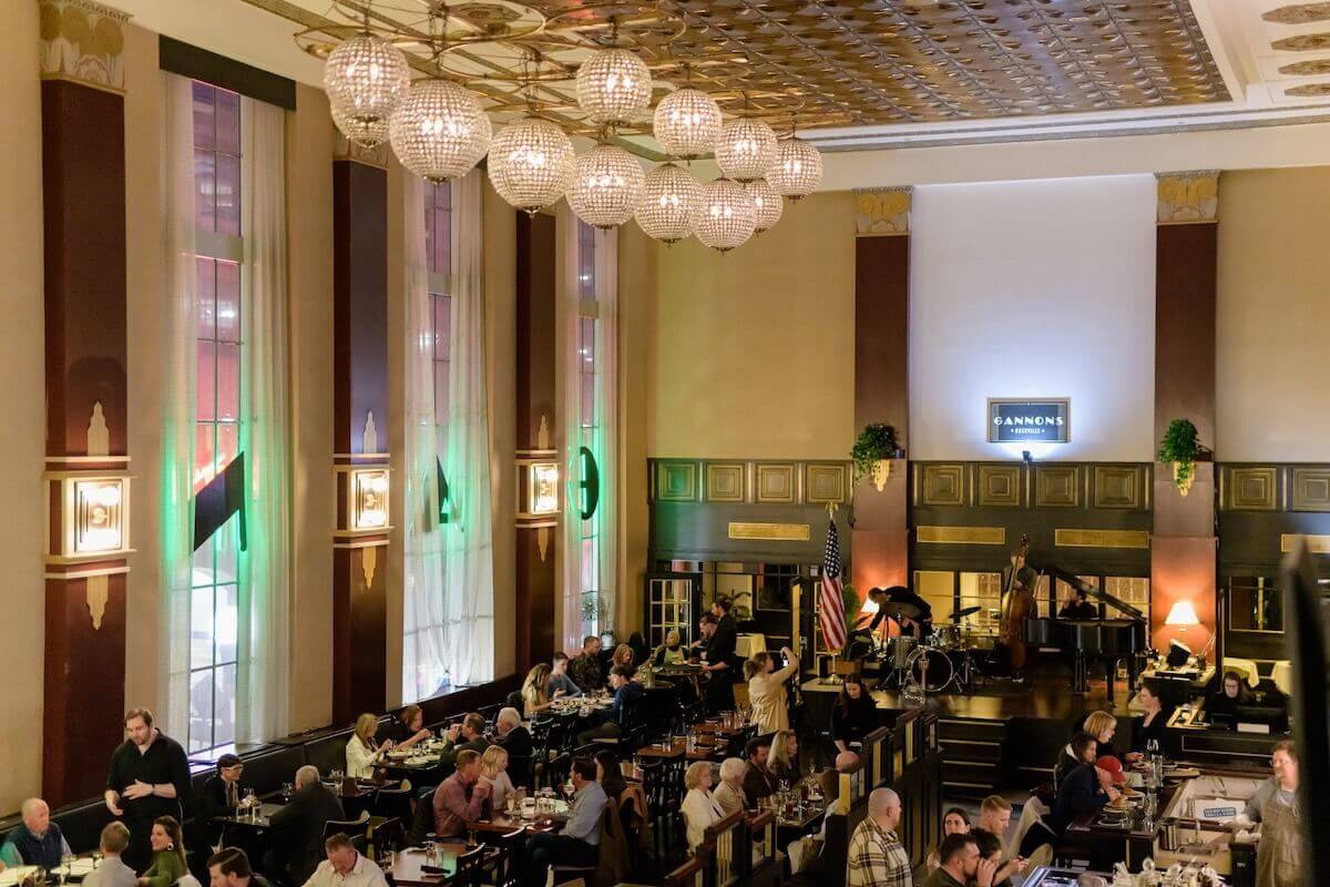 A large, elegant restaurant with high ceilings, chandeliers, and tall windows, filled with diners. A jazz band performs near a grand piano—an experience reminiscent of the top Nashville attractions.