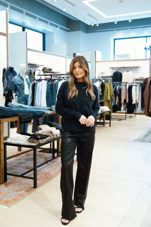 3 Franklin Boutiques Share Their Winter Wardrobe Favorites - 2 A woman wearing a black sweater and black leather pants stands in a Franklin boutique, surrounded by racks of clothes and folded garments, browsing for her winter wardrobe.