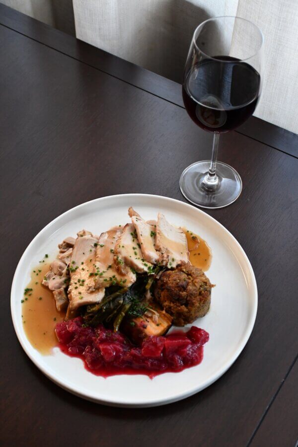 30+ Nashville Restaurants Open on Thanksgiving Day - 4 A plate of sliced turkey with gravy, stuffing, greens, and cranberry sauce is served with red wine on a dark wooden table—perfect for those seeking Nashville restaurants open on Thanksgiving.
