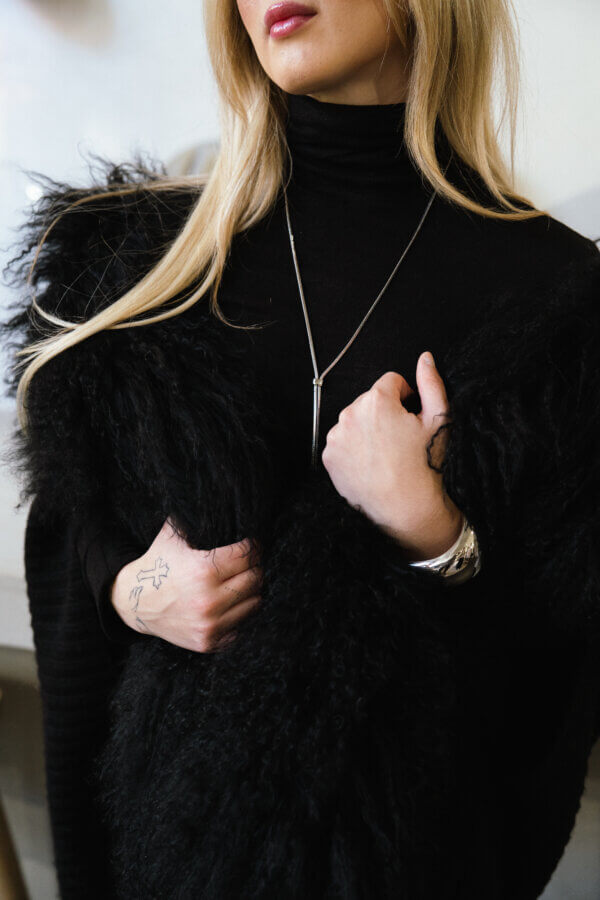 3 Franklin Boutiques Share Their Winter Wardrobe Favorites - 9 A woman with long blonde hair showcases chic winter fashion in a black turtleneck and fuzzy shawl, accessorized with a silver necklace and bracelet, plus a small tattoo on her hand—a stylish look perfect for your winter wardrobe.
