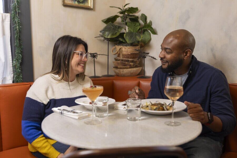 Two people sit at a restaurant table, enjoying a meal and drinks while facing each other and smiling, savoring Mississippi eats and sharing a true Southern tradition.