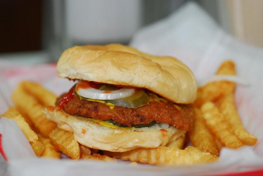 A fried chicken sandwich with pickles, onions, ketchup, and mustard—a true Southern Tradition—served with crinkle-cut French fries on a paper-lined tray.