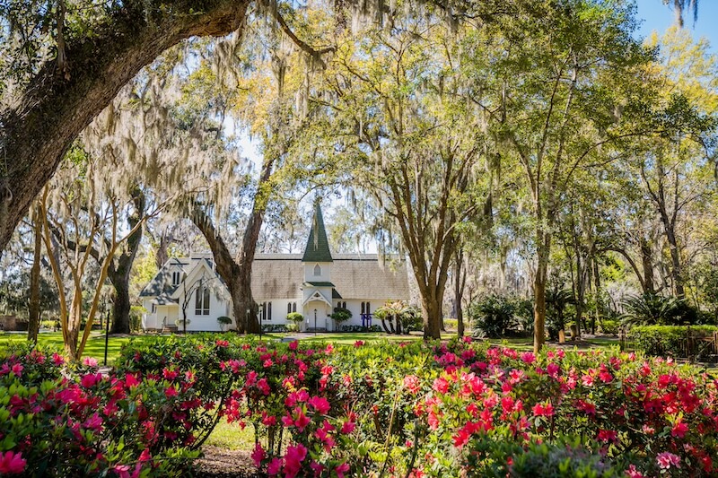 Can't-Miss 2026 Events in Georgia's Beloved Golden Isles - 5 A small white church with a steeple is surrounded by large trees and blooming pink flowers on a sunny day, offering a picturesque spot for travel photos and reflecting the charm of Golden Isles events in 2026.