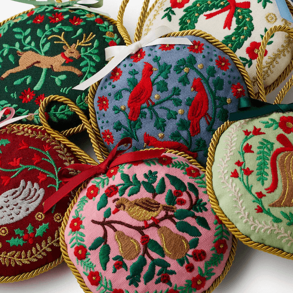 14 Southern Ornament & Stocking Shops We Love - 13 A collection of round, embroidered Southern ornaments with nature-themed designsβbirds, deer, and greeneryβeach edged with gold cord and decorated with small bows for a charming Southern Christmas.