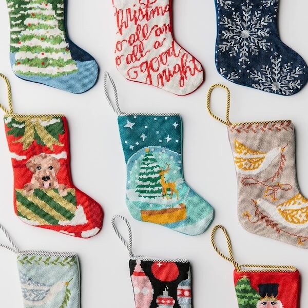 14 Southern Ornament & Stocking Shops We Love - 2 Nine small Christmas stocking ornaments, including southern ornaments with trees, animals, snowflakes, and festive text, are arranged in a grid on a white background.