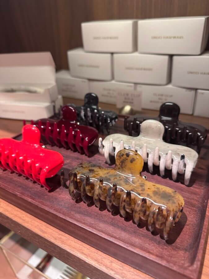 50 Under $50: Your Nashville Holiday Gift Guide - 18 Four large hair claw clips in red, maroon, black, white, and tortoiseshell rest on a wooden tray with boxed products behindβperfect for Gifts under $50 or as a chic pick from your Holiday Gift Guide.