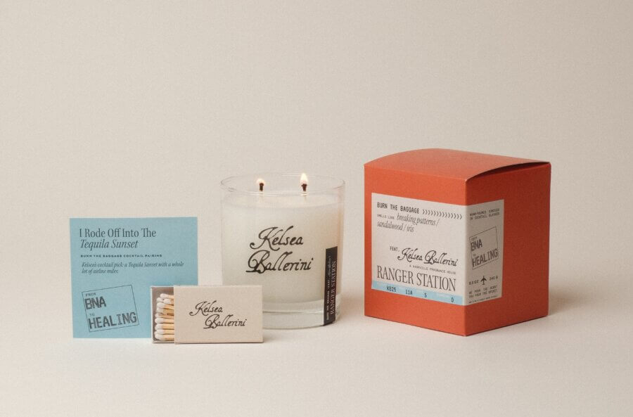 50 Under $50: Your Nashville Holiday Gift Guide - 10 A Kelsea Ballerini-branded candle with two wicks is displayed with a box of matches, a blue note card, and an orange box featuring product labelsβperfect for christmas gifts under $50.