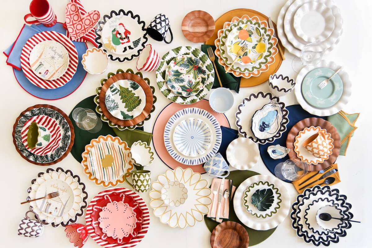 An assortment of colorful, patterned plates, bowls, and utensils from Laura Johnson’s Happy Everything collection arranged on a white surface—perfect for Home & Hosting, featuring various playful designs and shapes.