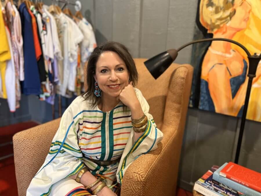 Birmingham's 10 Most Popular Articles of 2025 - 8 Woman in a striped dress sits in an armchair, smiling, surrounded by clothes on hangers and stacks of books.