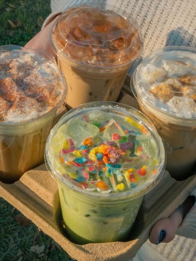 She's Behind One of BHAM’s Most Beloved Coffee Shops - 3 Four assorted iced drinks from Cala Coffee in plastic cups with lids, held in a cardboard tray; one topped with colorful cereal, others with whipped cream and spices from this popular BHAM coffee shop.