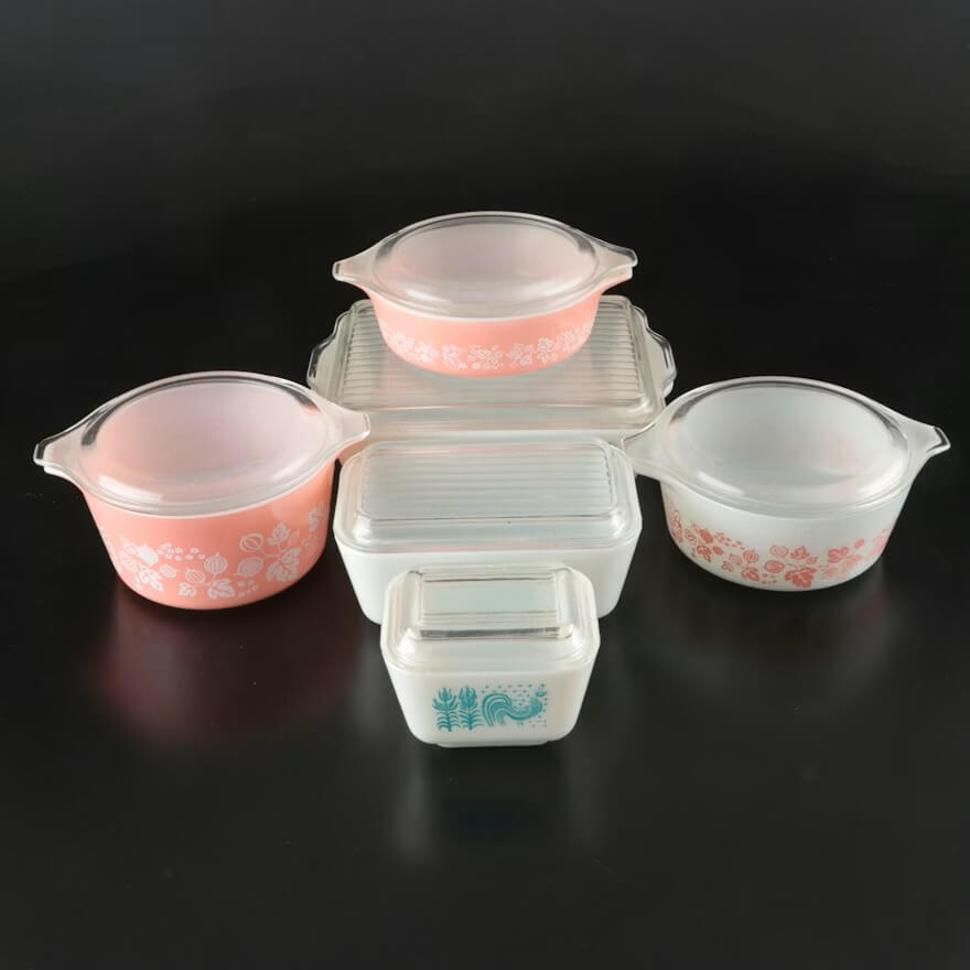 Stop Donating These 5 Items — They May Be Worth Serious Cash - 3 Five vintage glass Pyrex containers with lids—three with pink patterns, one blue, and one red—are arranged on a black background, perfect for anyone interested in collecting valuable items.