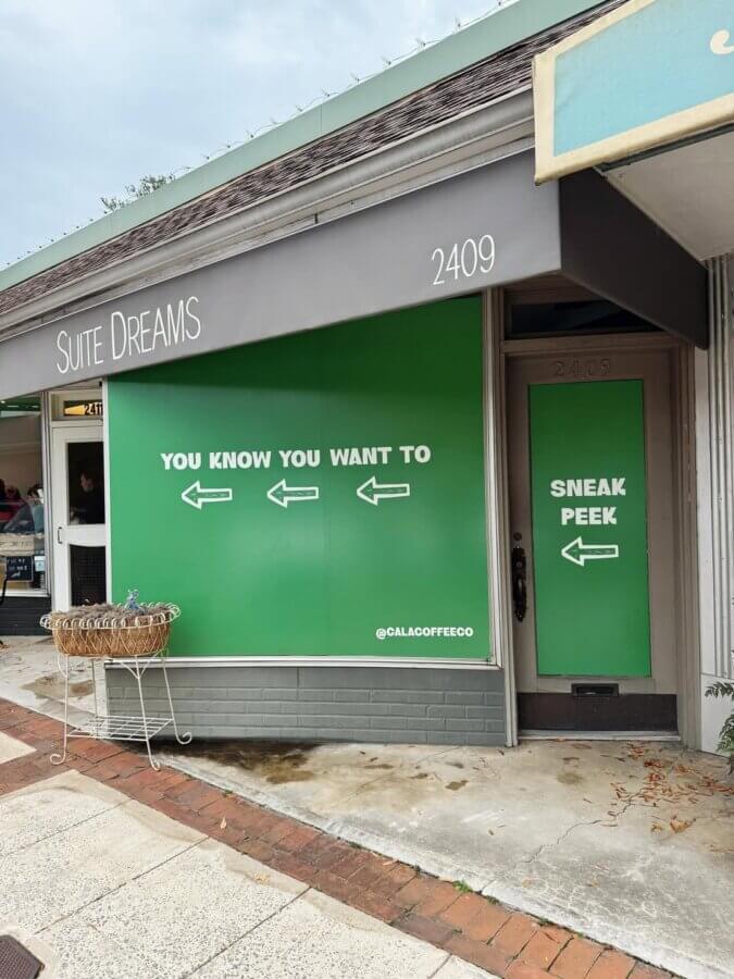 She's Behind One of BHAM’s Most Beloved Coffee Shops - 6 A storefront window and door display green signs with white text and arrows, reading "YOU KNOW YOU WANT TO" and "SNEAK PEEK".