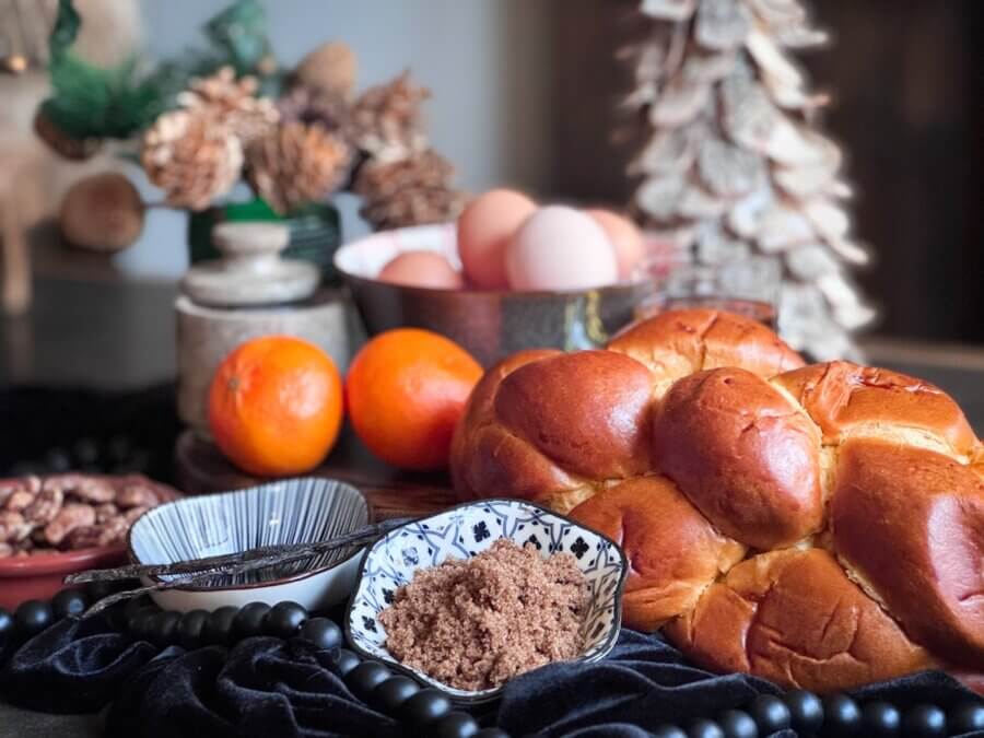 Eggnog French Toast Bake โ Perfect for the Holidays! - 2 A loaf of braided bread, brown sugar, oranges, eggs, and pecans are arranged on a table with decorative pine cones and a wooden treeโperfect ingredients for whipping up Overnight French Toast or experimenting with Cooking Unscripted.