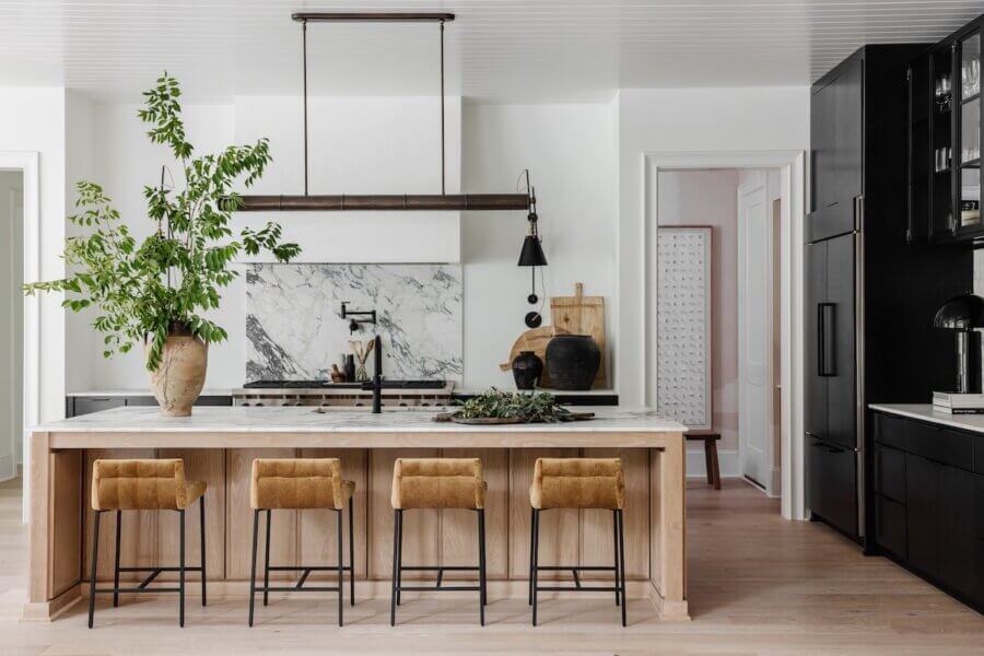 A Charlotte Home Bathed in Light, Texture, and Modern Romance - 8 Modern kitchen with a marble island, four tan barstools, black cabinetry, a large potted plant, and a marble backsplash.
