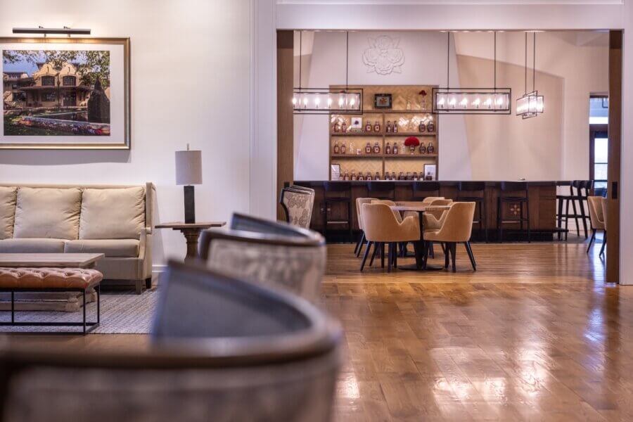 Are These Kentucky's Most Beautiful Distilleries? - 9 Spacious hotel lounge with cushioned chairs, a sofa, a framed picture on the wall, and a bar area showcasing spirits from some of the best distilleries, with shelves and seating in the background.