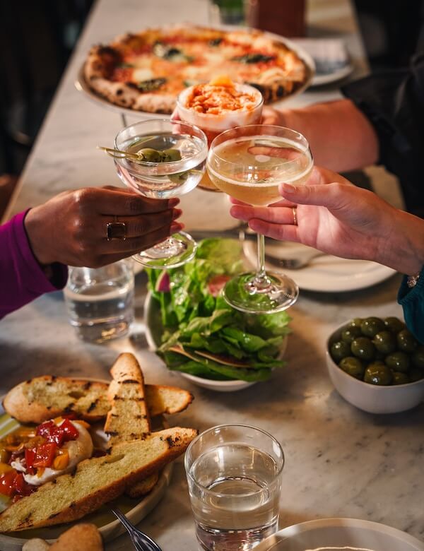 8 Mississippi Destinations Worth the Drive - 2 Three people clink glasses over a table with pizza, salad, bruschetta, green olives, and waterβsavoring memorable moments together like those found on unforgettable Mississippi travel adventures.
