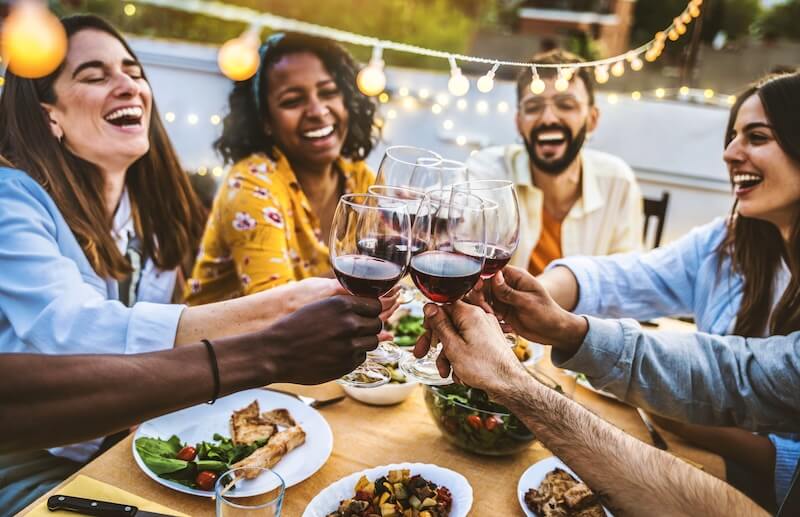 8 Mississippi Destinations Worth the Drive - 15 Five people sit around a table with food, clinking wine glasses and sharing memorable moments outdoors under string lights.