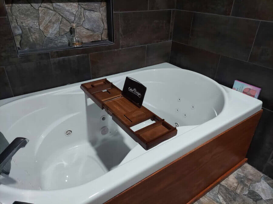 The Best Day Spas in Memphis for a Blissful Escape - 4 A white whirlpool bathtub with a wooden bath caddy sits in a dark-tiled bathroom; perfect for those seeking pampering Memphis experiences, with a book and small bottle nearby to inspire relaxation like the best spas Memphis offers.