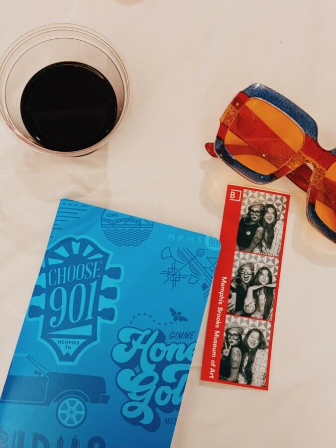 She Sees Magic in Every Corner of Memphis - 7 A cup of dark beverage, orange sunglasses, a blue "Choose 901" booklet, and a photo booth strip from Memphis Brooks Museum of Art.