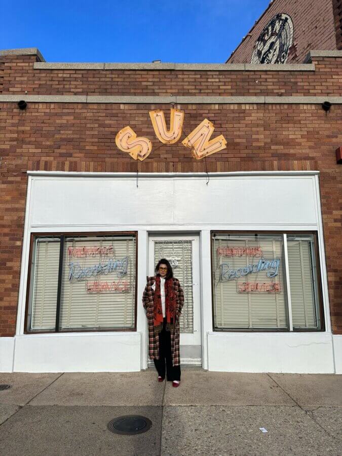 She Sees Magic in Every Corner of Memphis - 5 Mara Daniele stands in front of a brick building with a sign that reads "SUN" and neon "Recording Service" signs in the windows.