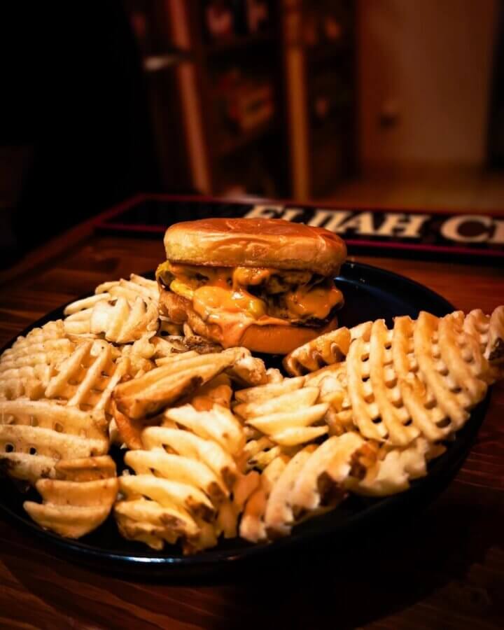 A cheeseburger sits on a plate surrounded by a large serving of waffle fries on a wooden table, offering a classic taste of Hermitage dining that any local guide would recommend among Hermitage restaurants.