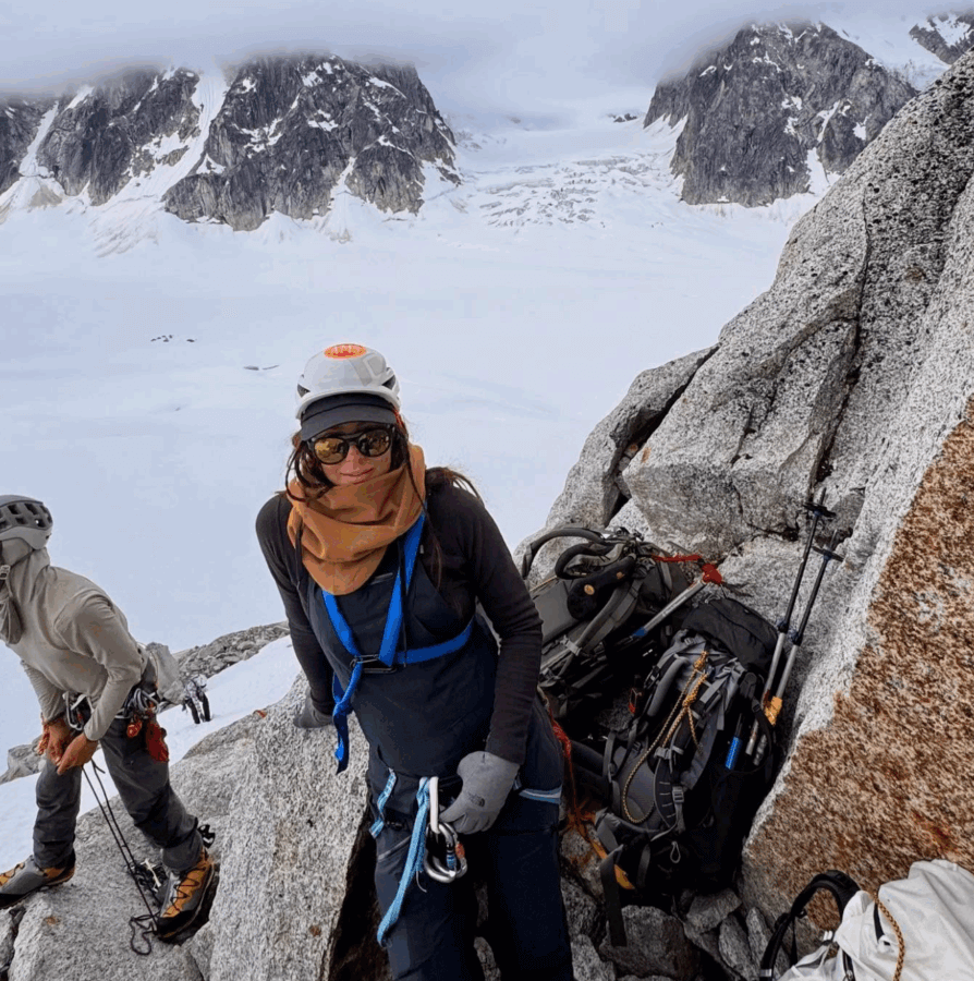 Meet the Woman Behind Old Glory & ELEVEN11 - 5 Two climbers stand on a rocky mountain slope with snow and glaciers in the background, wearing helmets, sunglasses, and climbing gear—capturing the adventurous spirit of Alexis Soler.